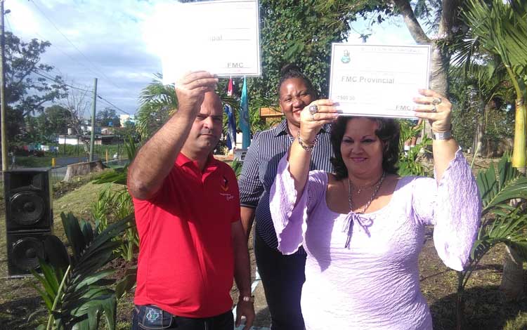 Osnay Miguel Colina, primer secretario PCC en Santa Clara, y Mayelín Díaz Rodríguez, del secretariado provincial FMC, muestran el bono simbólico recibido por el cumplimiento del Día de la Defensa de la Patria por un grupo de boques de la FMC.