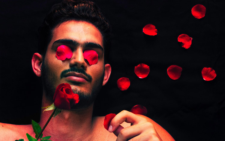 Joven con flor y ojos tapados por pétalos.