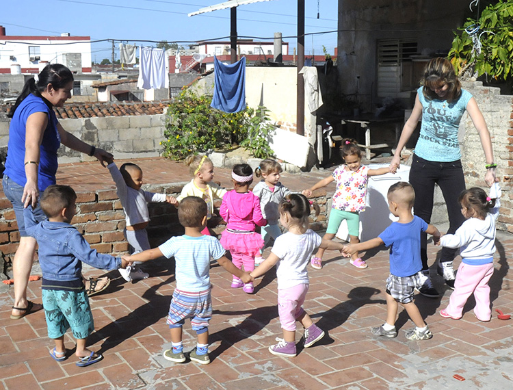Niños con sus cuidadoras juegan a la ronda.