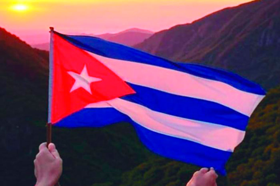 Manos sostienen una bandera cubana ,de fondo montañas
