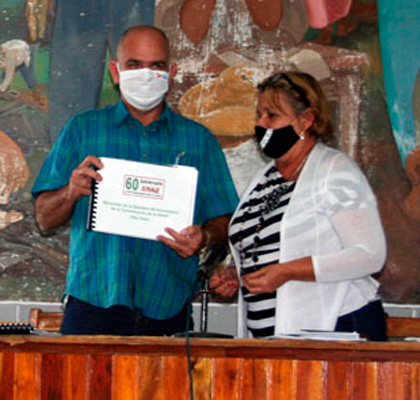 Betsy Arroyo Rafuls, presidenta de la ANAP en Villa Clara, entrega álbum de fotos del recorrido de la bandera Aniversario 60 de la ANAP.