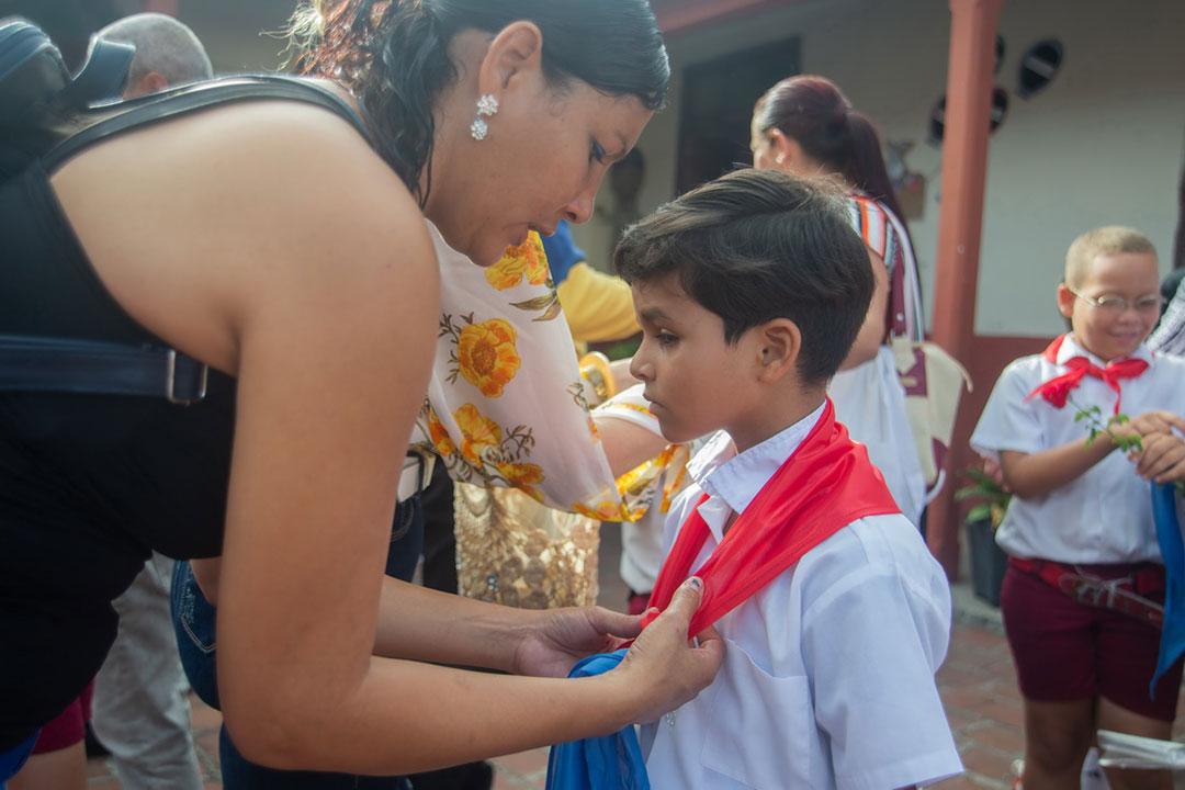 Madre coloca pañoleta roja a su hijo.